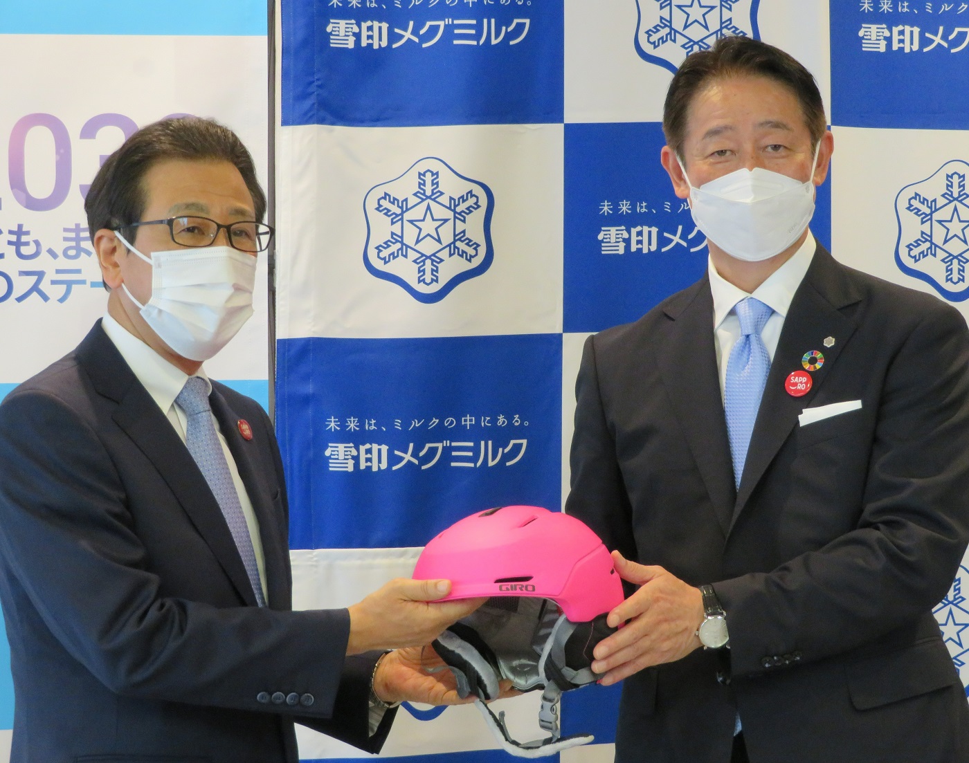 ヘルメットを手渡す佐藤雅俊雪印メグミルク社長（右）と秋元克広札幌市長