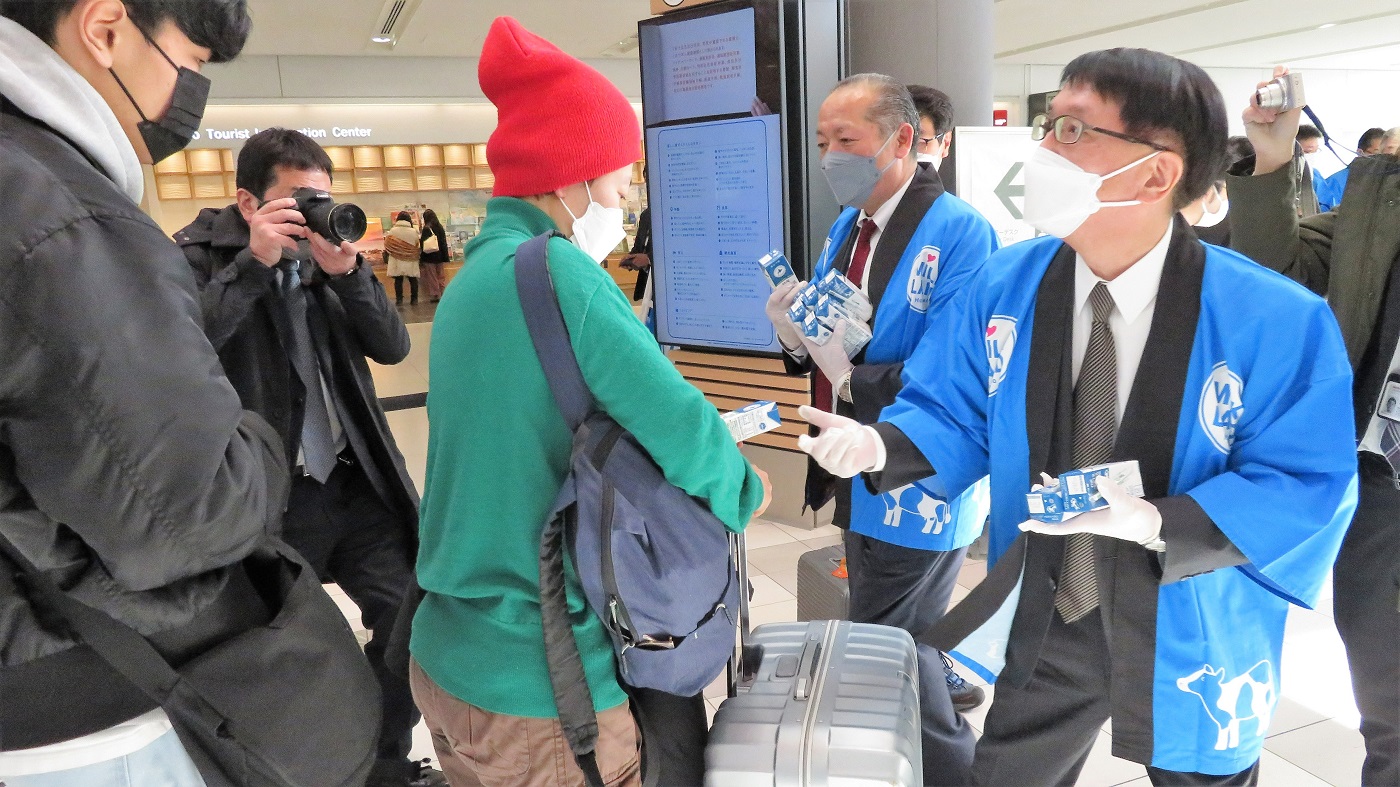 外国人旅行客に牛乳を手渡す安田北洋銀行頭取（右）と 西川ホクレン副会長（新千歳空港国際線ターミナル）