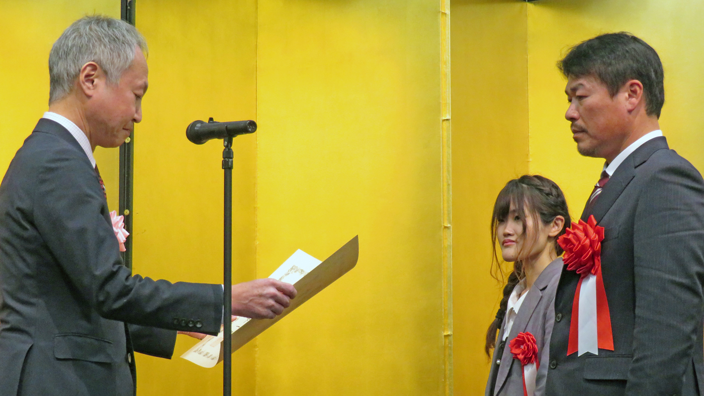 農水省の渡邉洋一畜産局長（左）から賞状を授与される丸山昭博・都々子夫妻