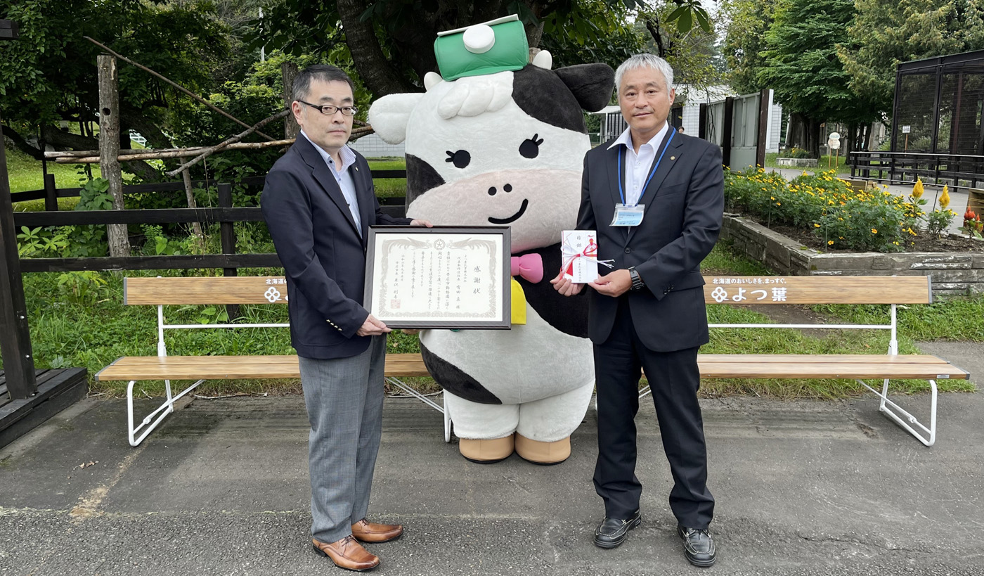 帯広市からの感謝状を手にする蔵田英正よつ葉総務広報グループ部長（左）と稲葉利行おびひろ動物園園長。後ろが同社寄贈のベンチ