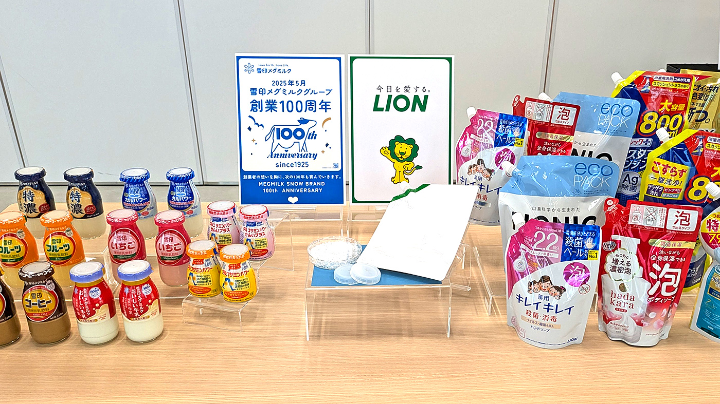 牛乳キャップから作られる包装容器の見本(中央手前)と両社の製品