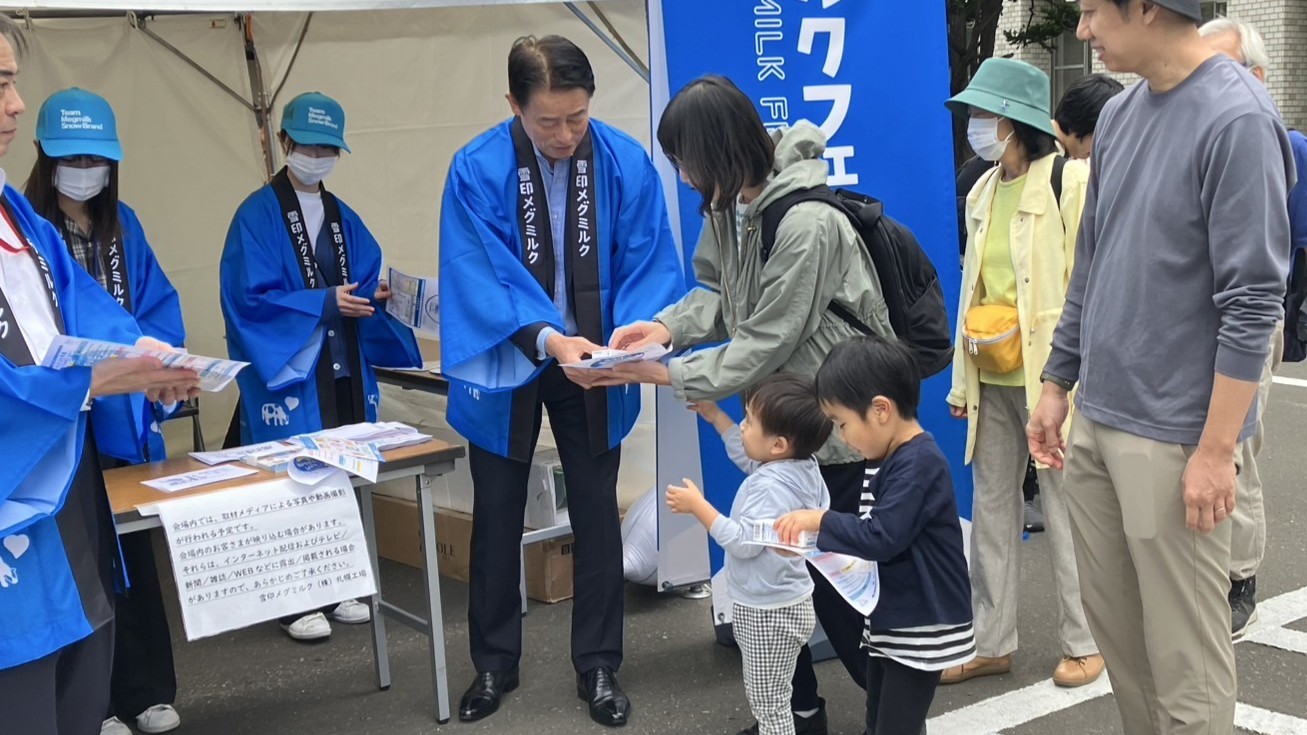 来場者にLL牛乳などを手渡す佐藤雅俊社長（中央）