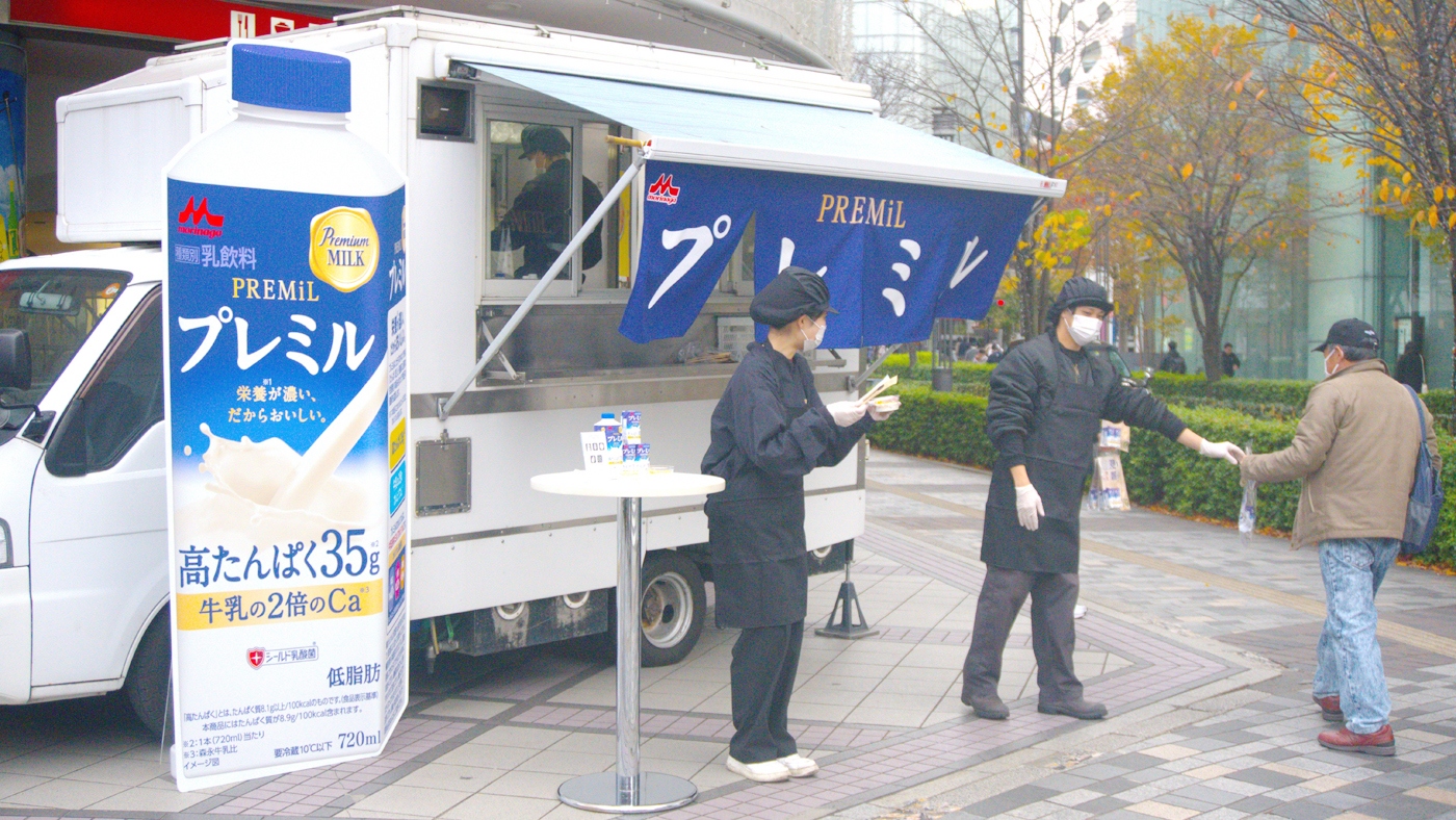 キッチンカーの前で「プレミル」のサンプルを受け取る通行人