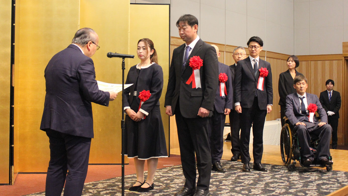 壇上で表彰される藤田貴良さん、麻奈美さん夫妻