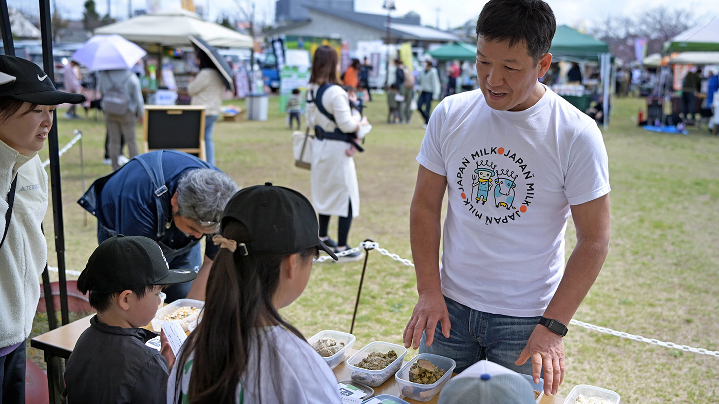 酪農について、子どもたちにエサを使って説明する切替宣充さん（右端）ら