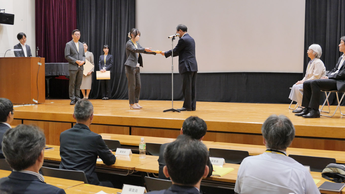 消費・安全局長賞の受賞者を代表して沖田賢治審議官（壇上右）から表彰状を受け取る十勝家畜保健衛生所の担当者