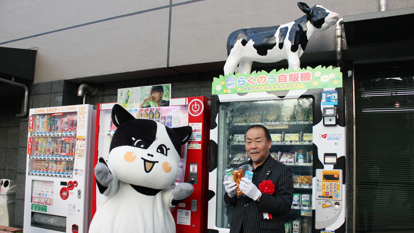 自販機で買った乳飲料やチーズを手にする隈部洋会長